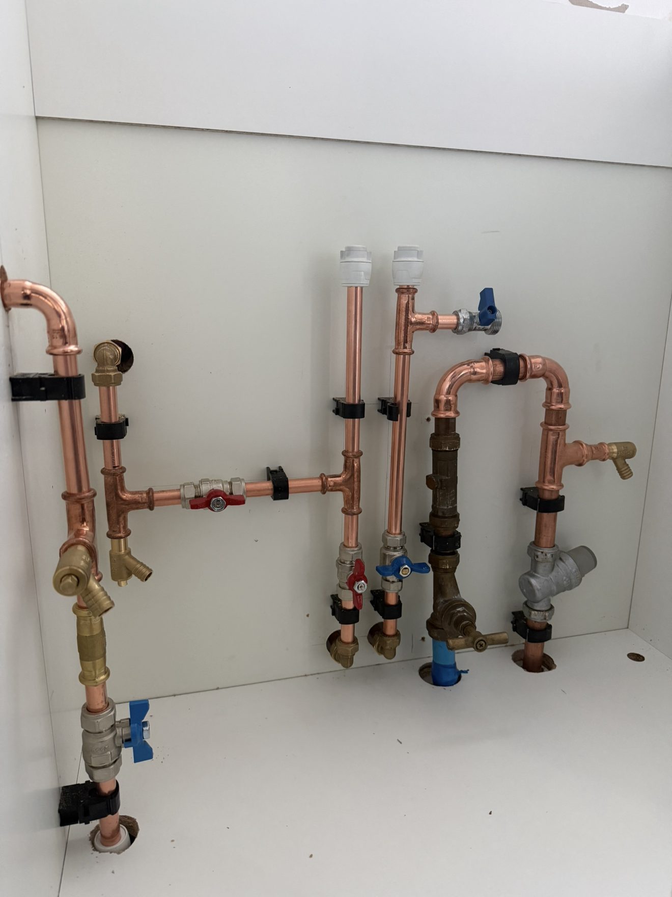 First and second fix plumbing with neatly clipped copper pipework under a sink unit